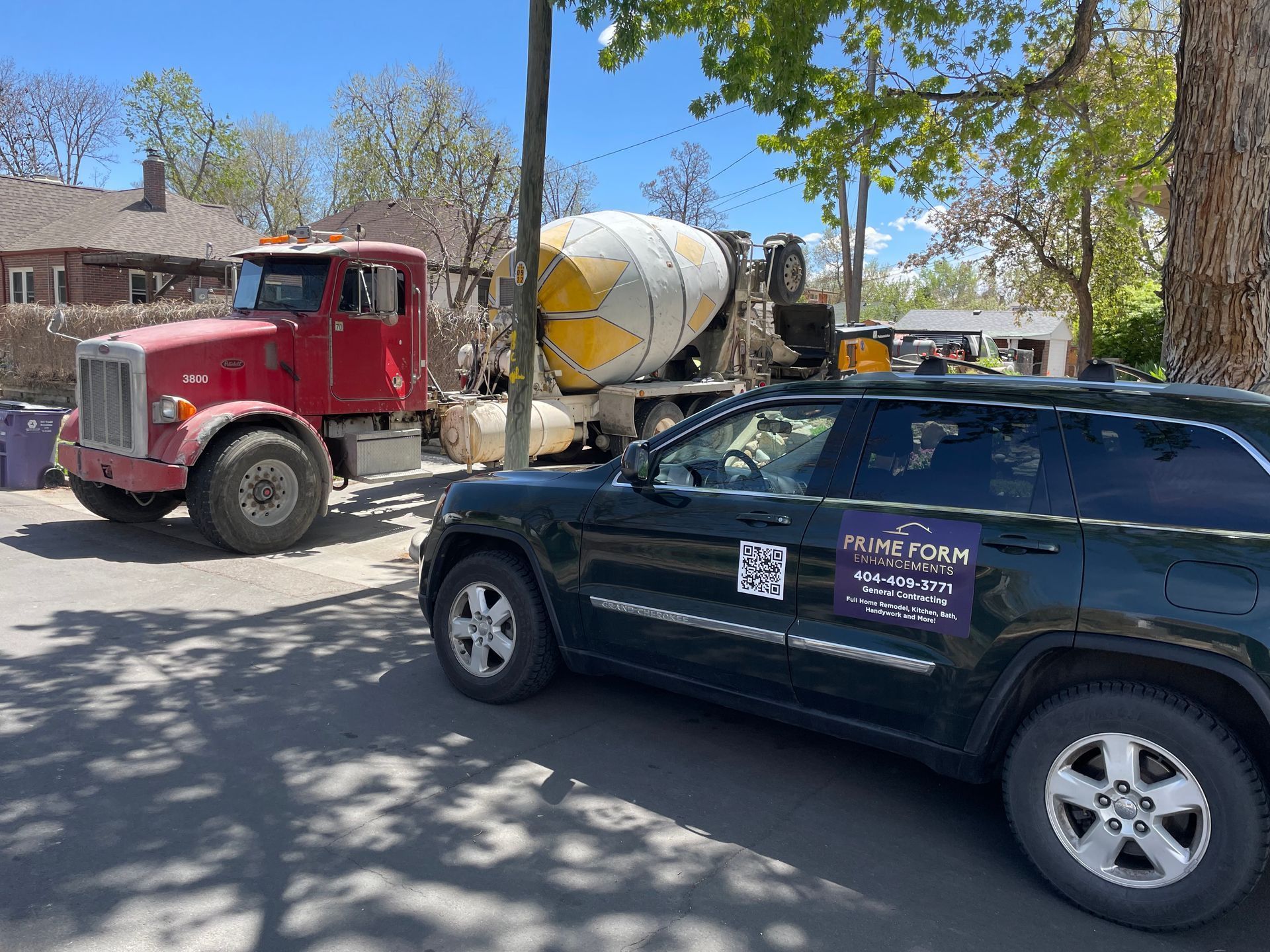 Red cement truck and dark SUV parked on a street near a house.