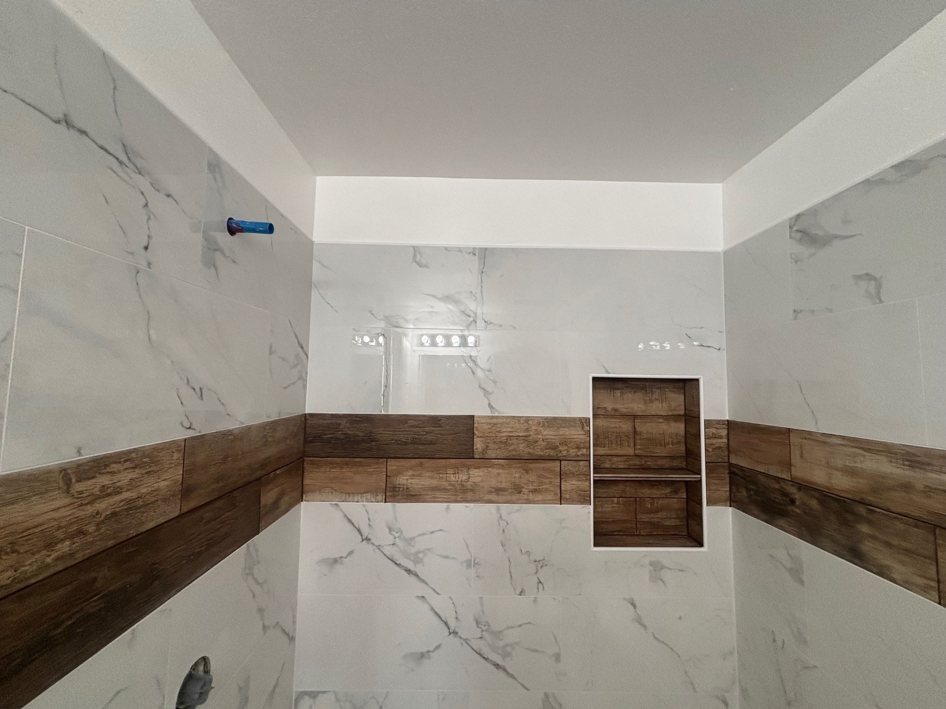 Bathroom with white and brown tiled walls, a recessed shelf, and a blue pipe.