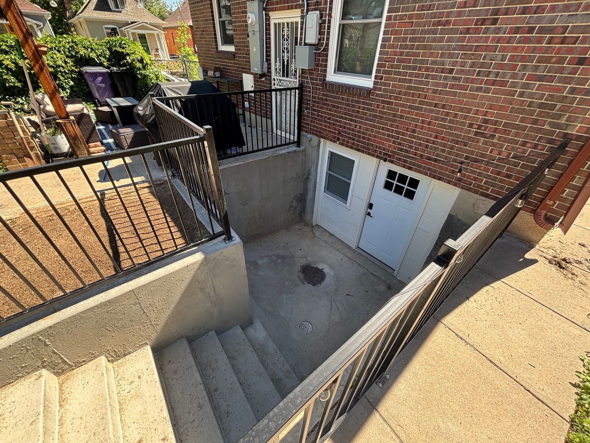 Concrete staircase leading down to a basement entrance with a white door. Black railings frame