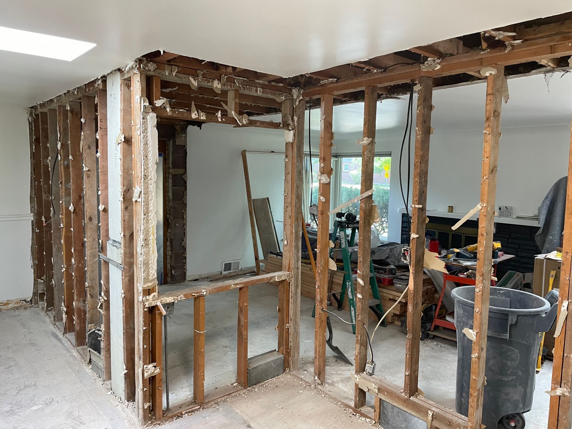 Interior room undergoing renovation; exposed wooden studs, drywall removed. Debris on floor, visible work tools.