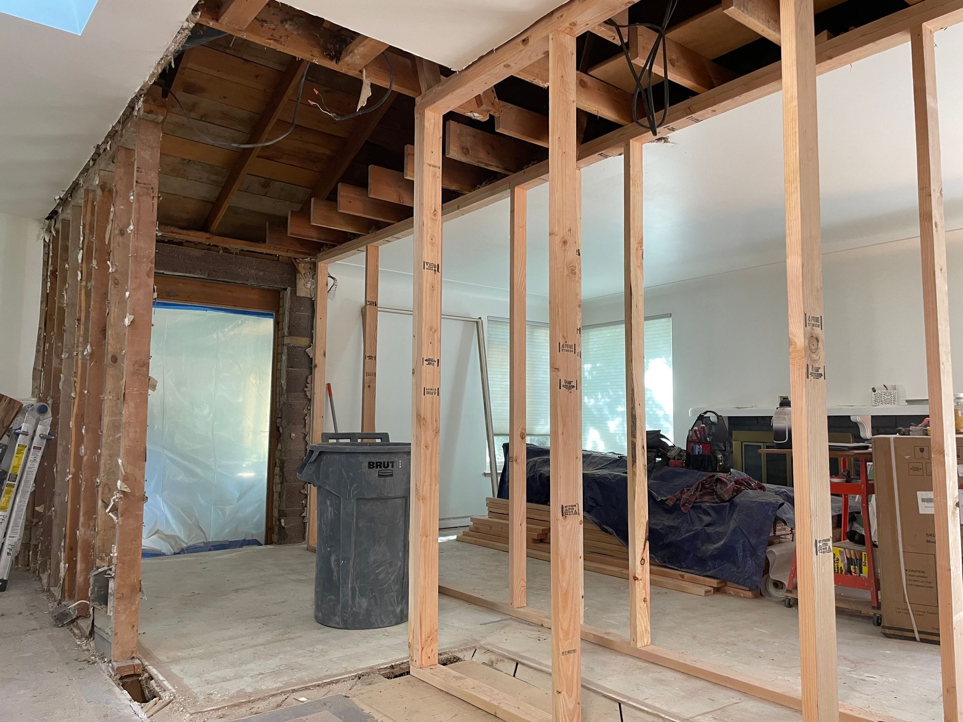 Interior renovation in progress: exposed wooden framing, trash can, unfinished walls, doorway, and debris.