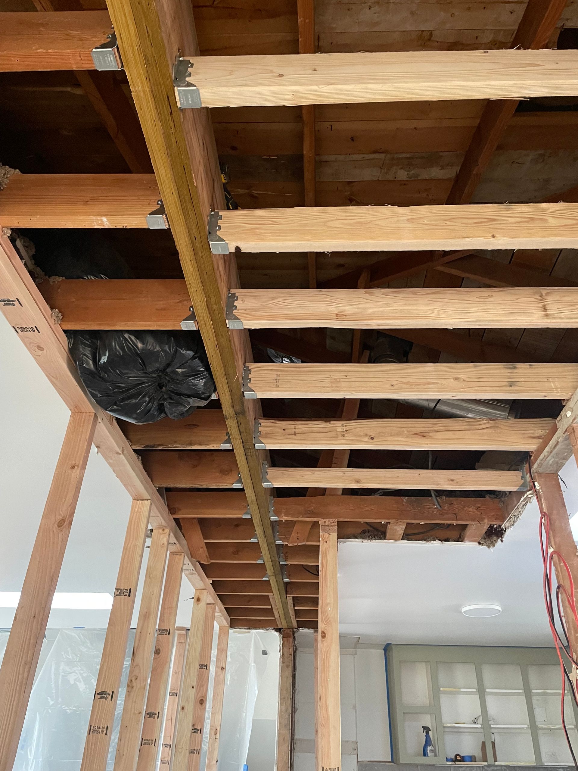 Construction site: exposed wooden beams, ceiling, and wall studs. Black debris bag in an open space.