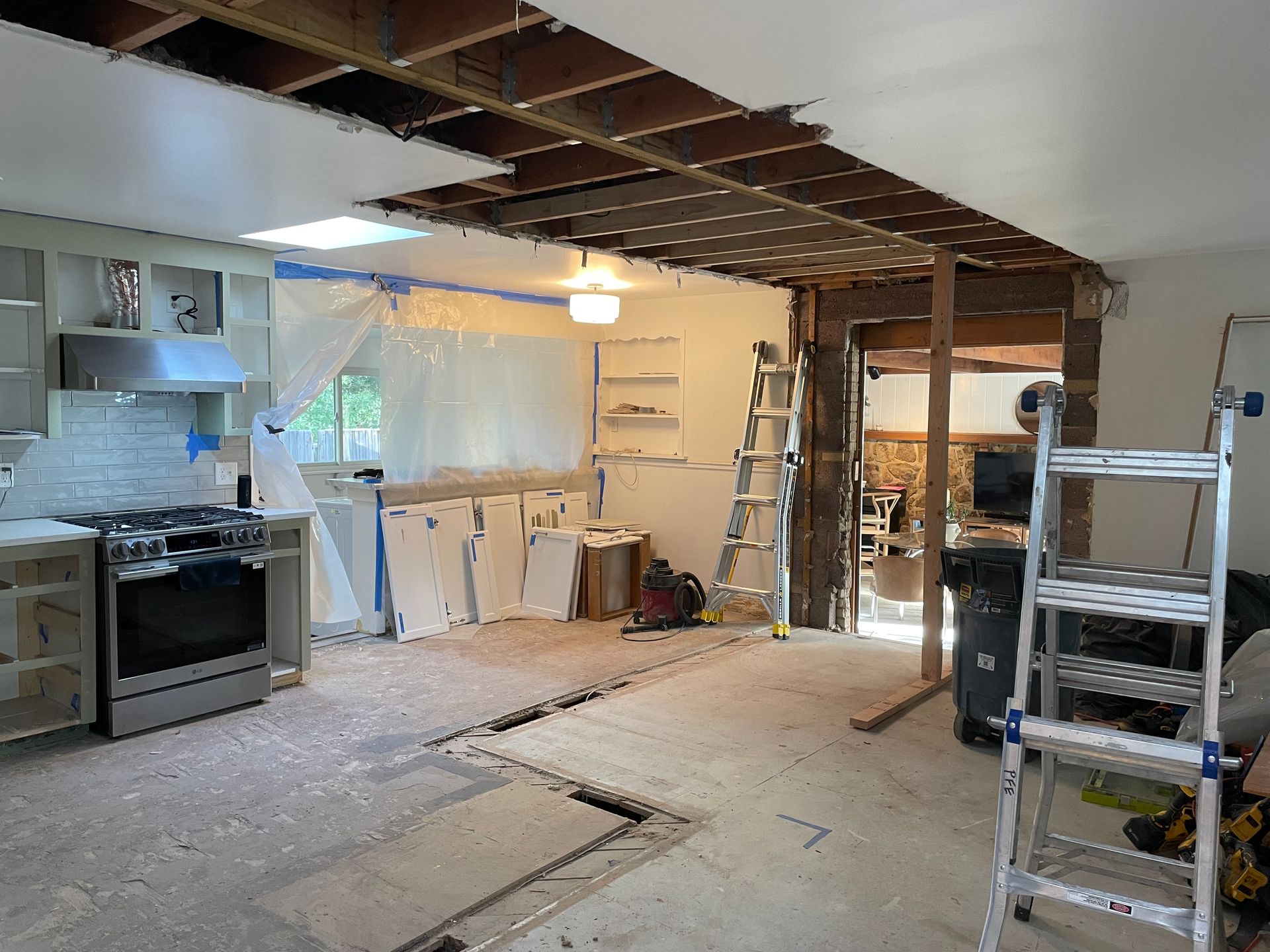 Kitchen under renovation; ceiling and floor partially removed; appliances remain.