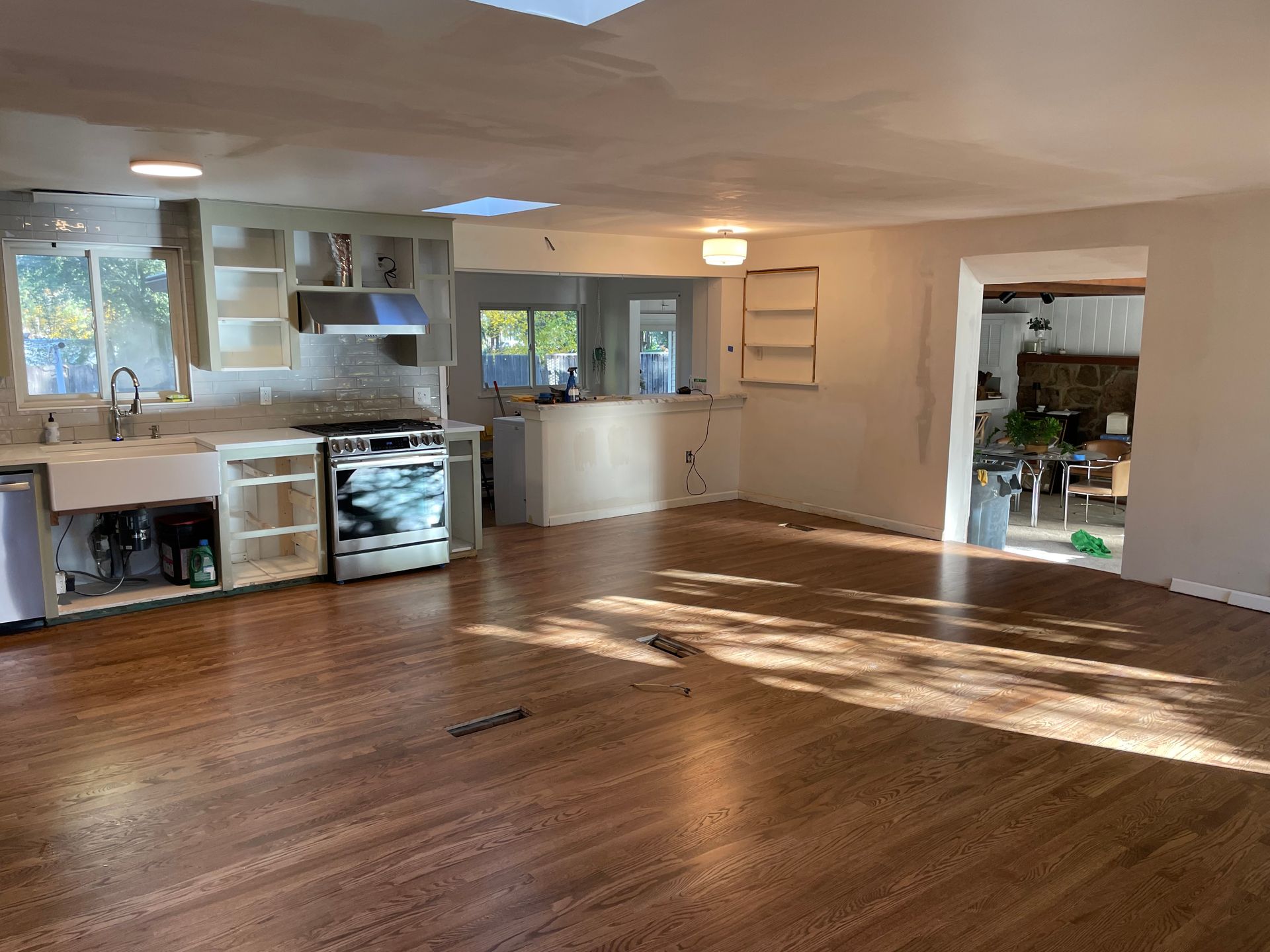 An open-concept kitchen and living space during renovation, with exposed cabinetry, wood floors, and natural light.