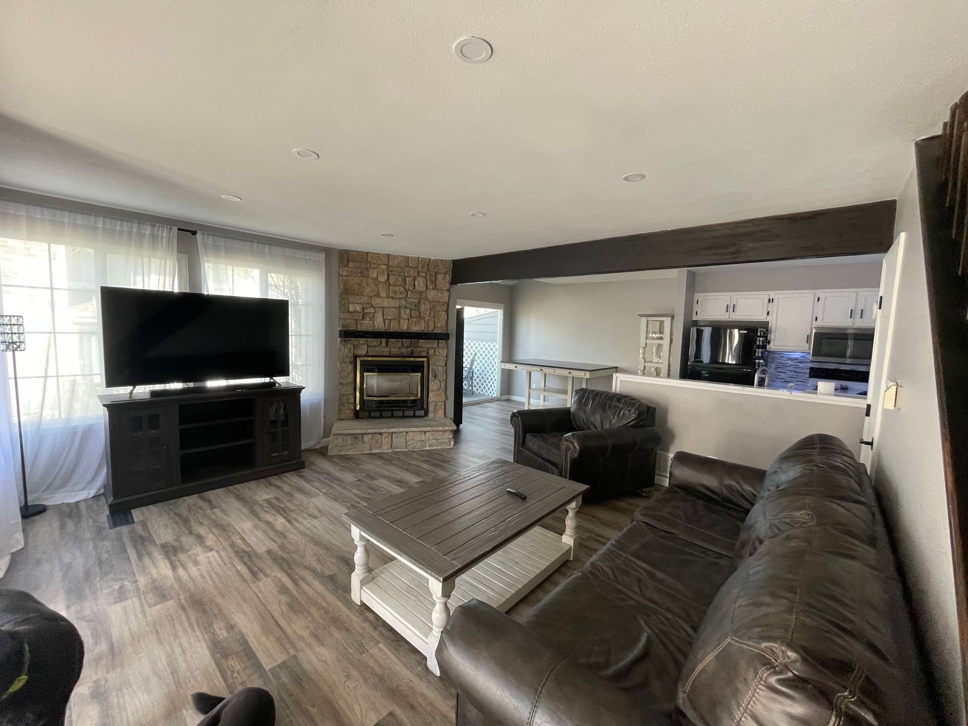 Living room with TV, fireplace, couch, and chair. Open to a kitchen area.