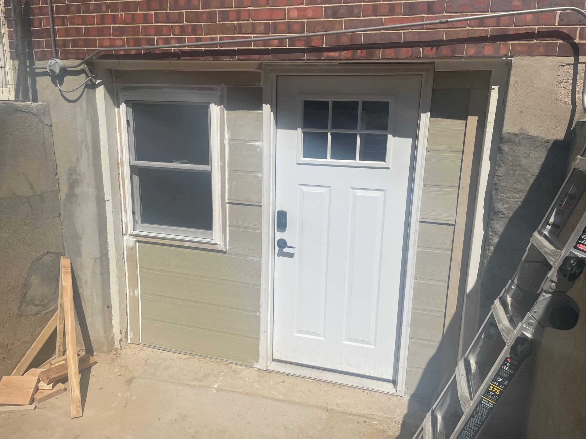 Exterior door and window in a brick and concrete wall. White door with glass panes, green siding.