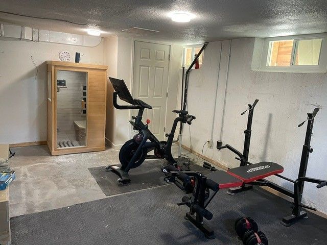 Basement gym with stationary bike, weight bench, and sauna. Concrete floor, white walls.