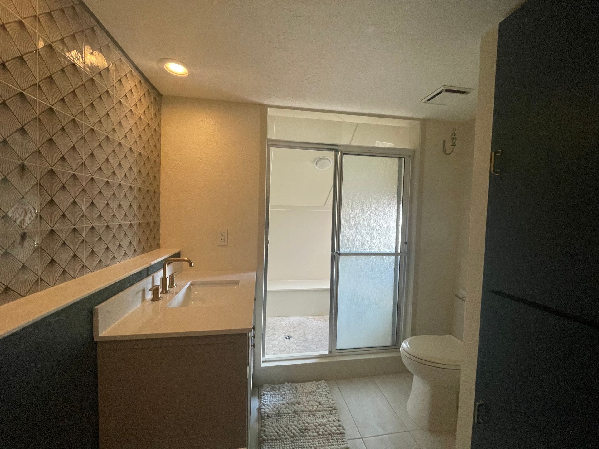 Bathroom with light-colored vanity, patterned accent wall, glass shower, and toilet.