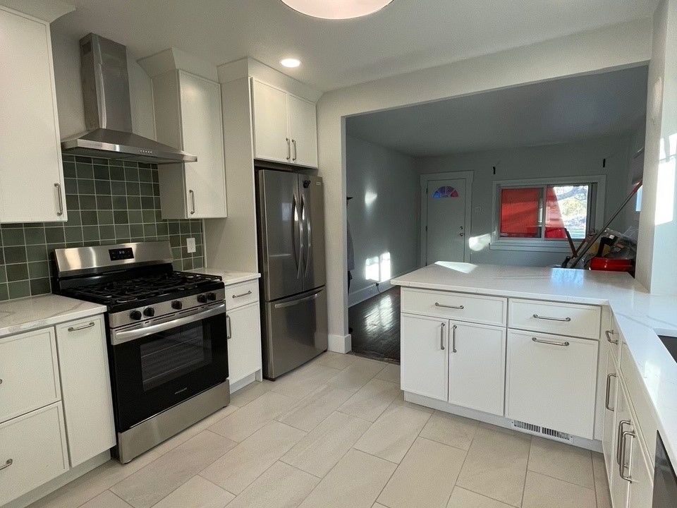 Modern kitchen with white cabinets, stainless steel appliances, and gray-green tile backsplash.