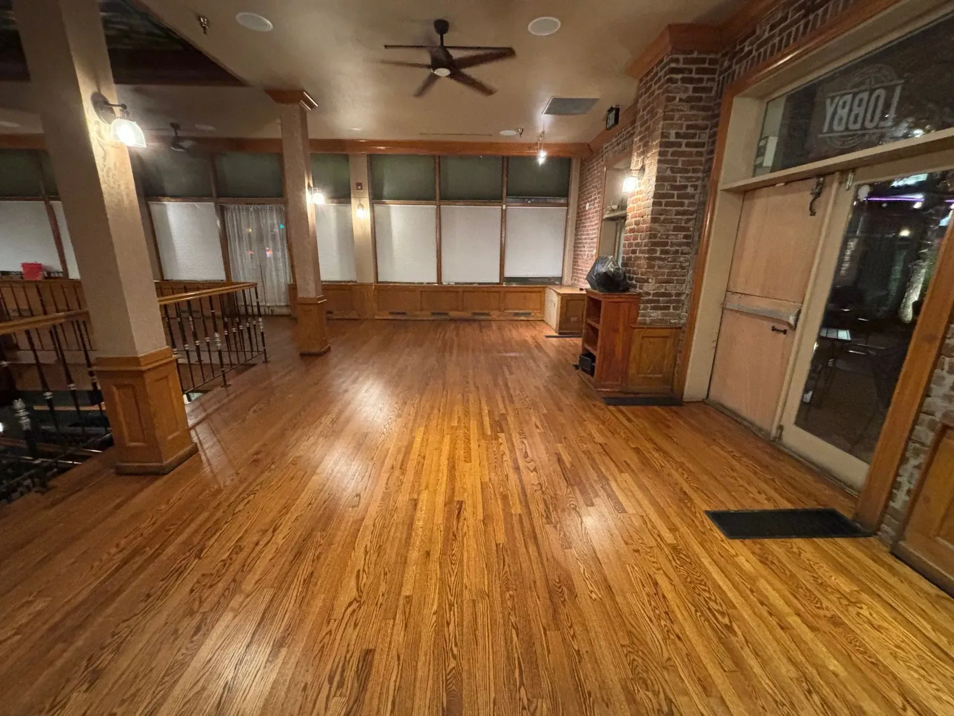 A spacious room with hardwood floors and exposed brick walls.  A doorway reads 
