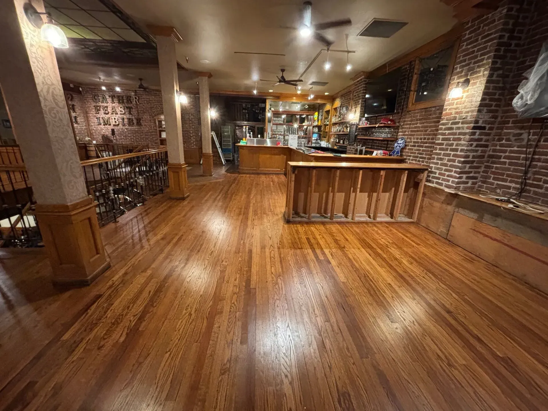 Interior of a bar with wooden floors, exposed brick walls, a bar counter, and tables. The lighting is dim.