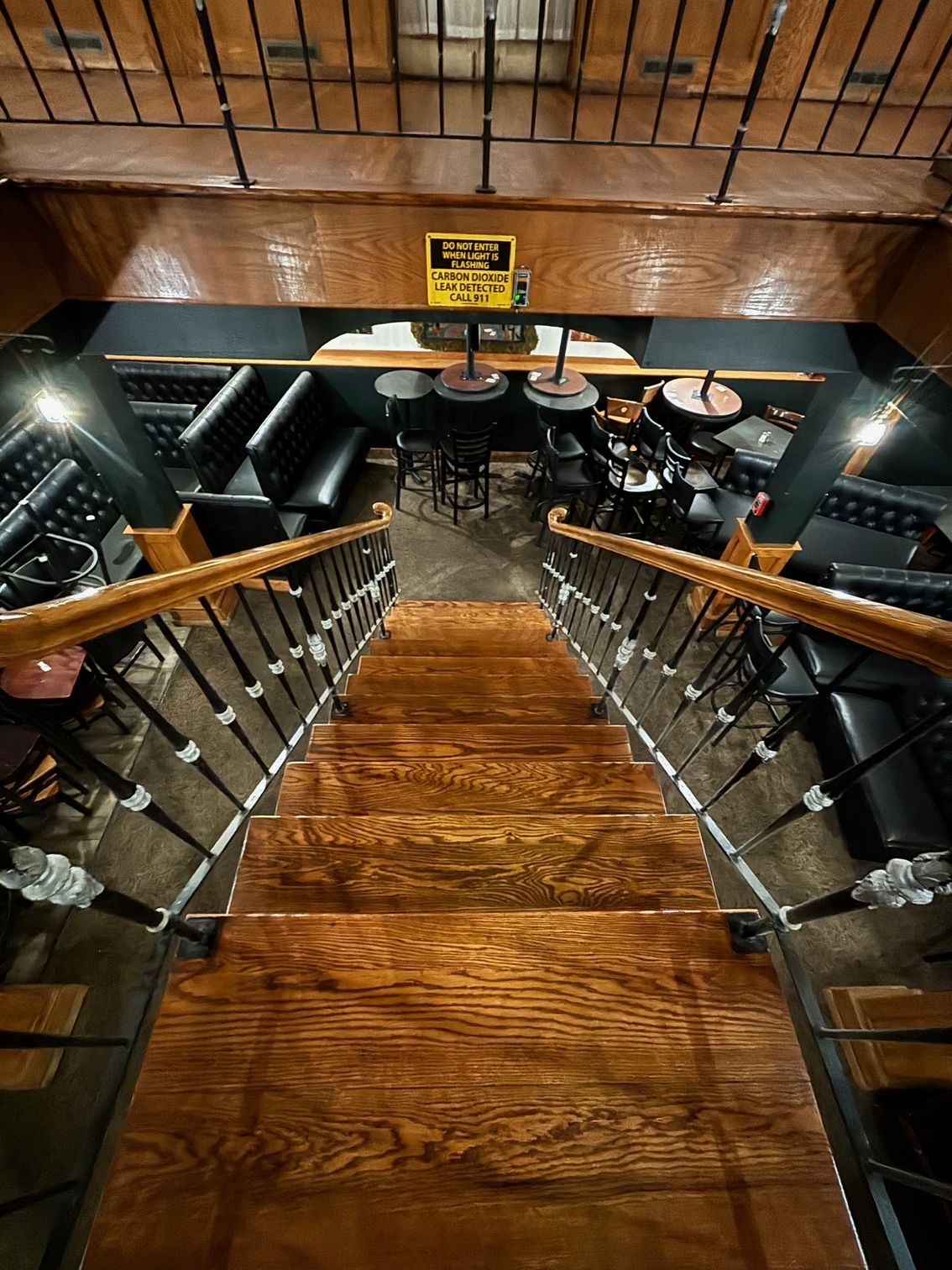 Wooden staircase leading down to a dimly lit bar area with black booths and small tables.