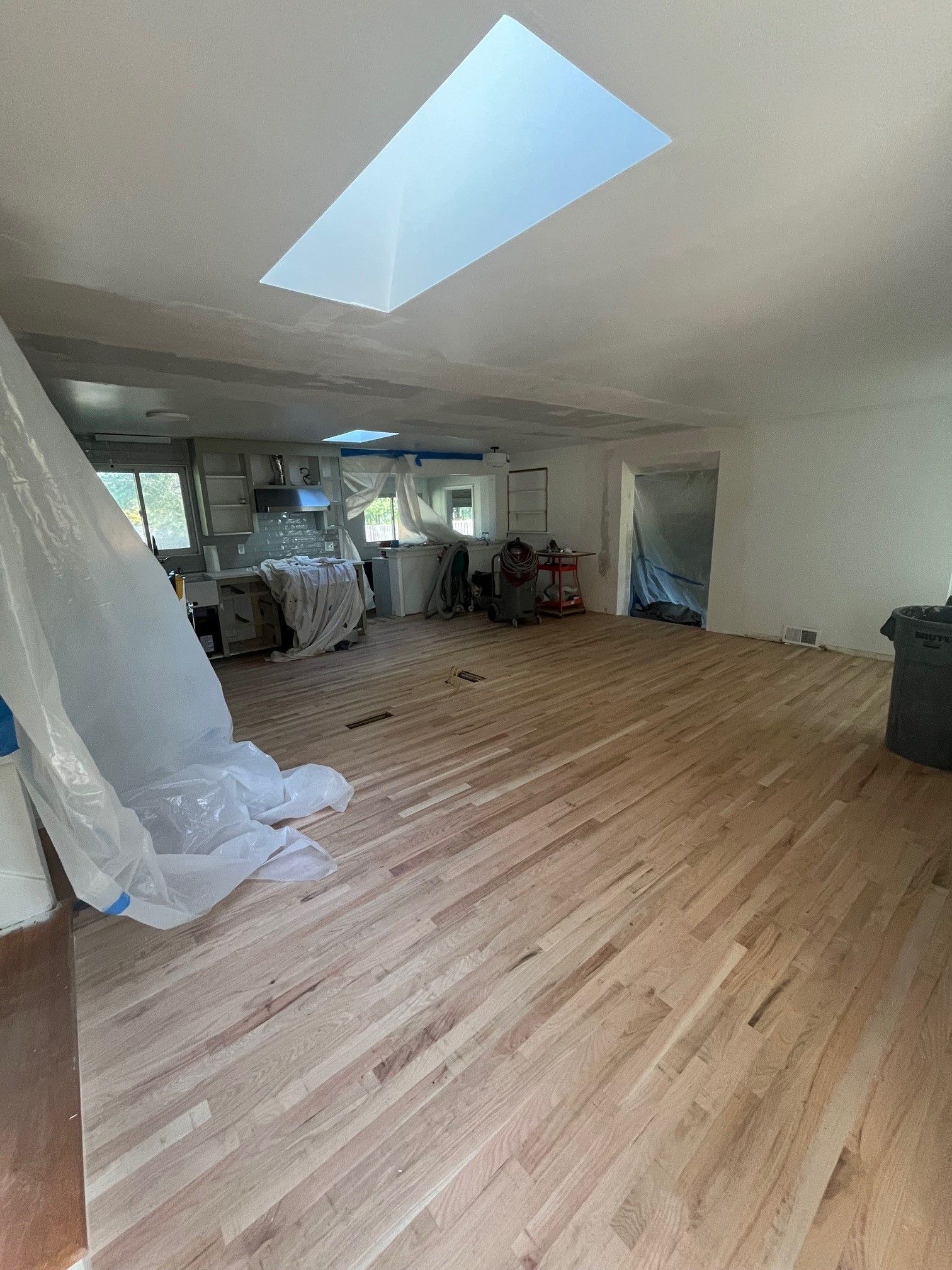 Interior renovation. New hardwood floor. Kitchen in the background is covered in plastic. Skylight in the ceiling.