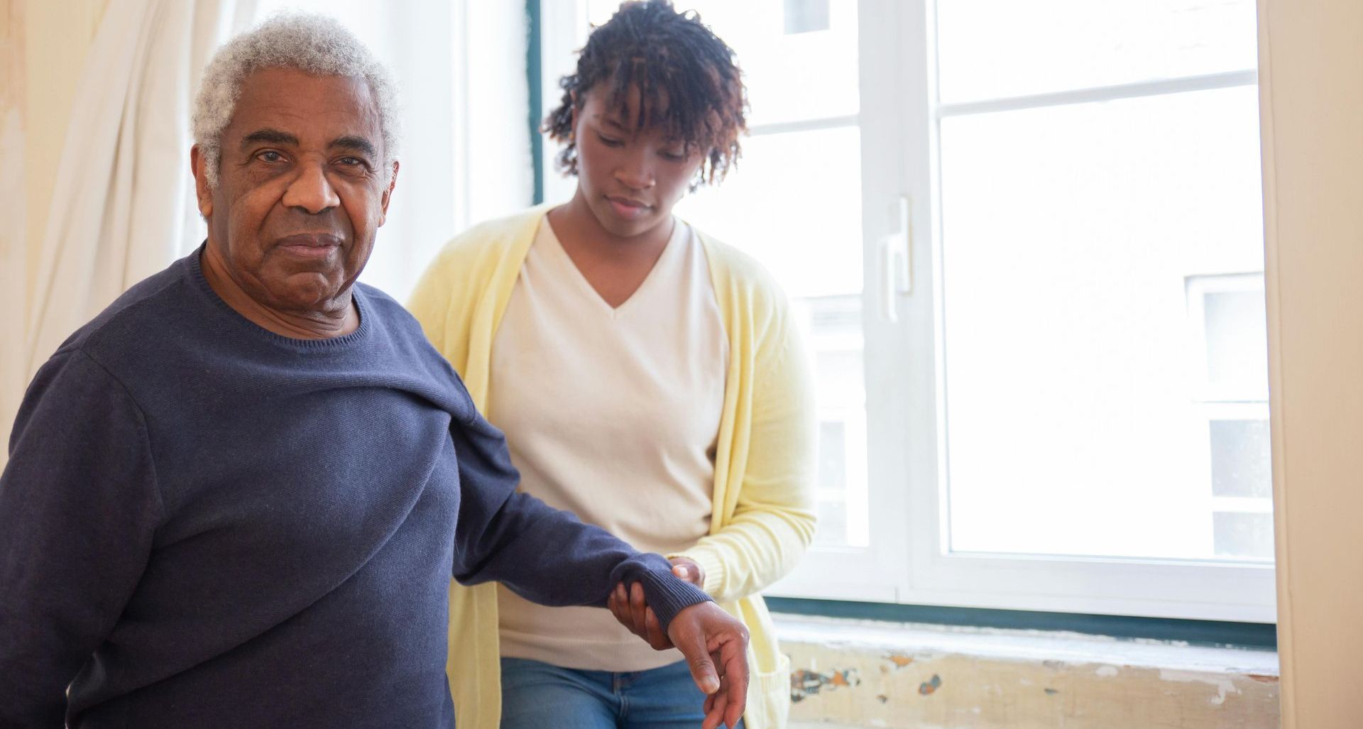A woman is helping an elderly man walk in a room.