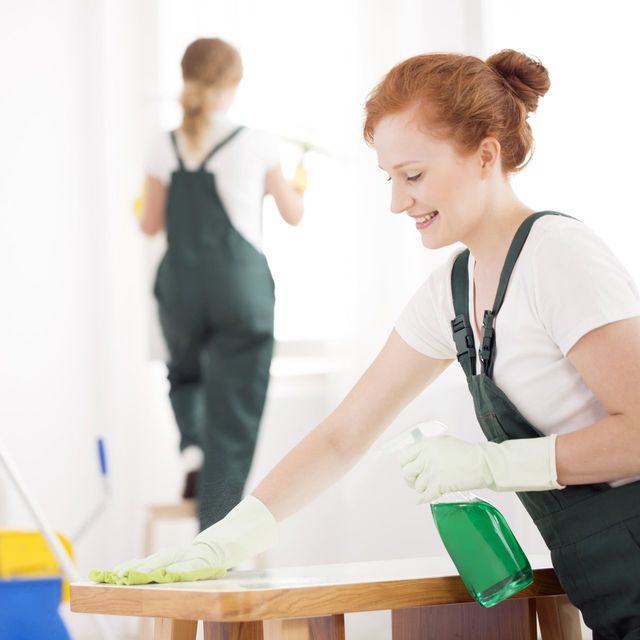 A woman in green overalls is cleaning a table