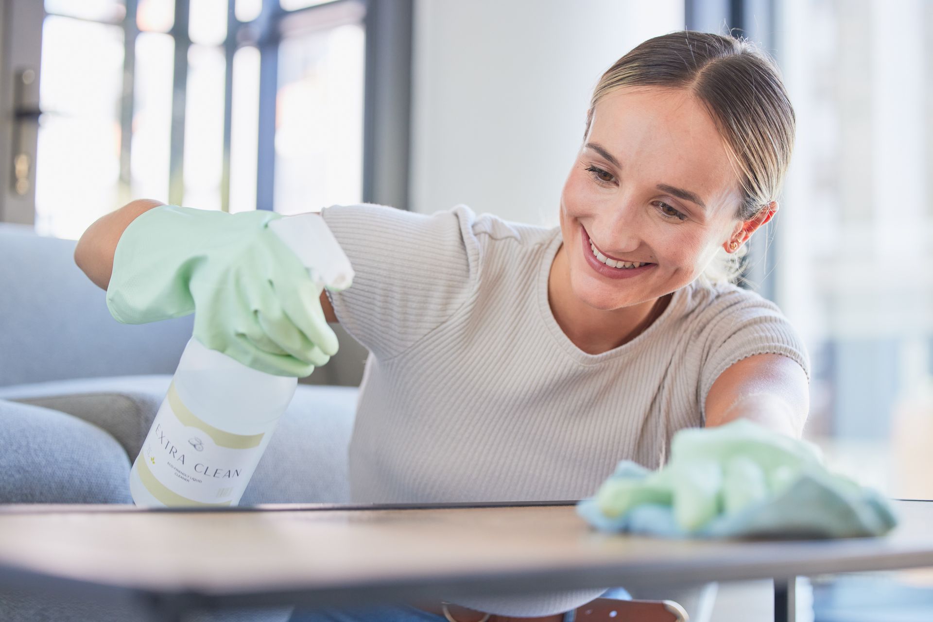 A woman is cleaning a table with a spray bottle and a cloth.