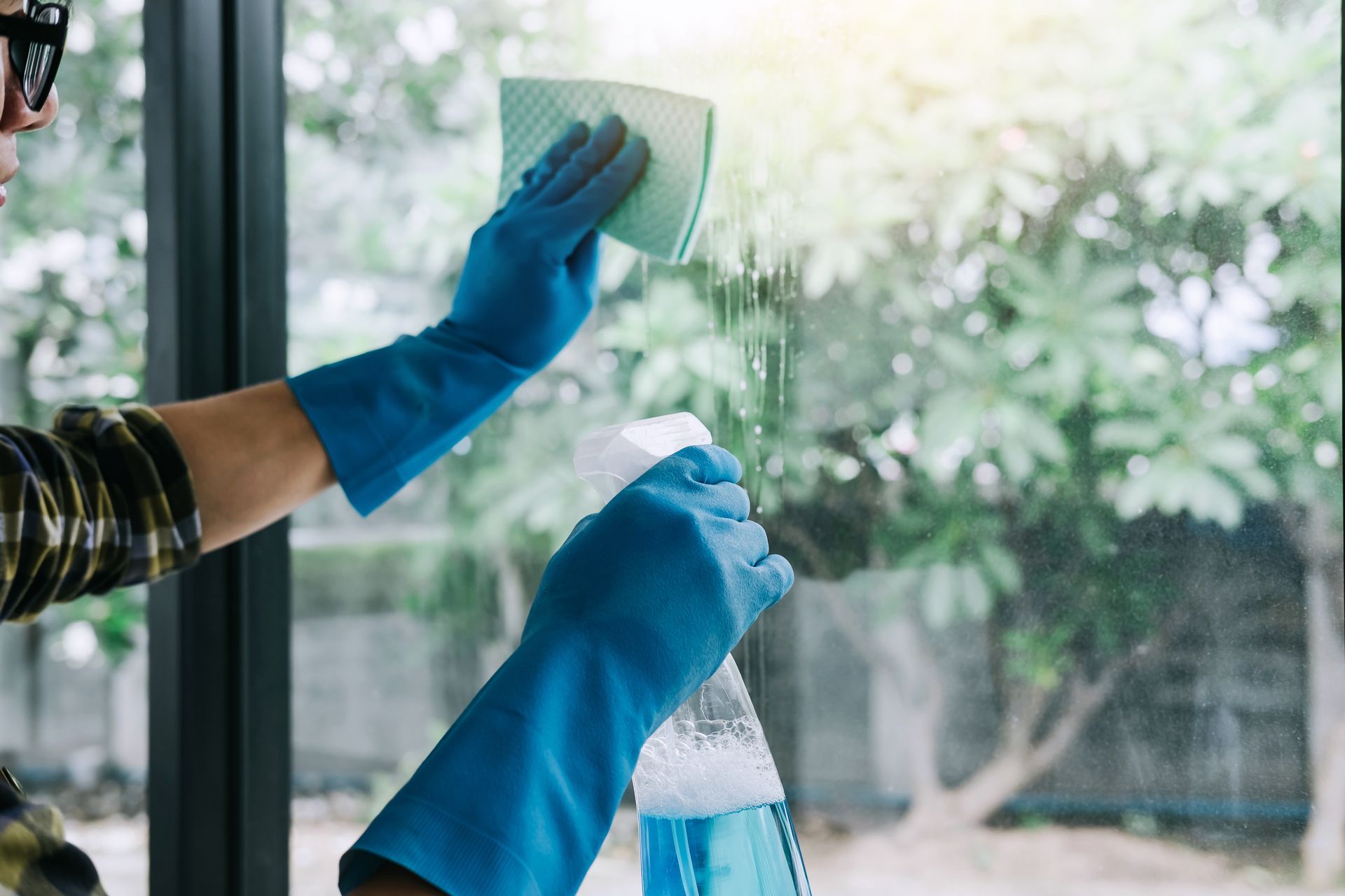 A person wearing blue gloves is cleaning a window with a sponge.