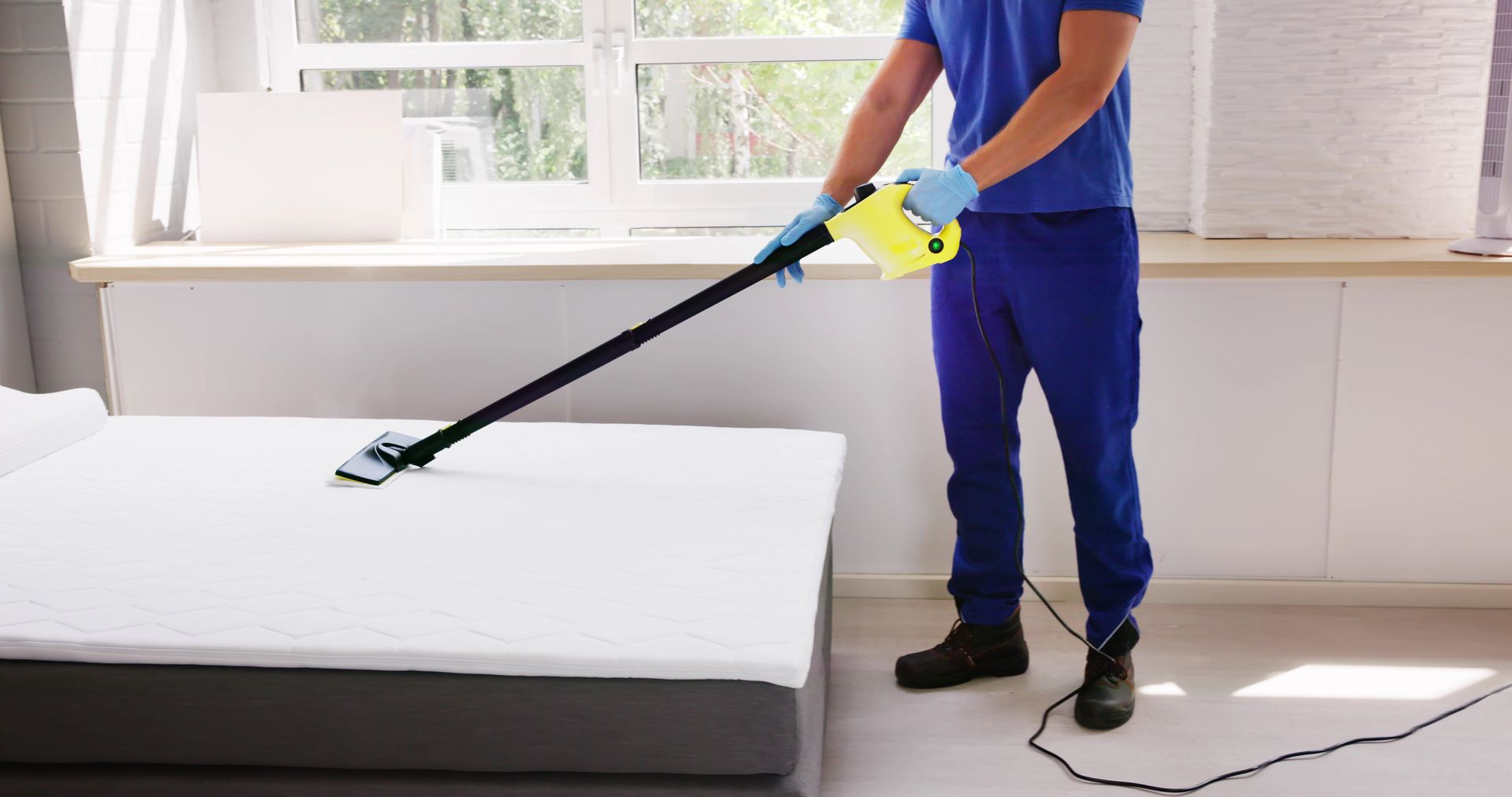 A man is cleaning a mattress with a vacuum cleaner.