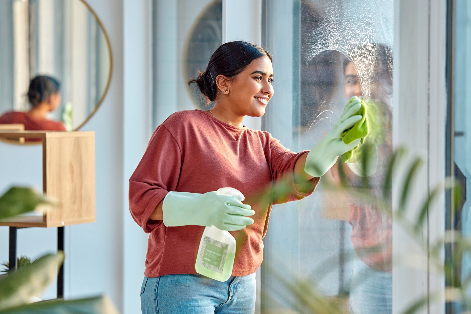 A woman is cleaning a window with a spray bottle and a cloth.