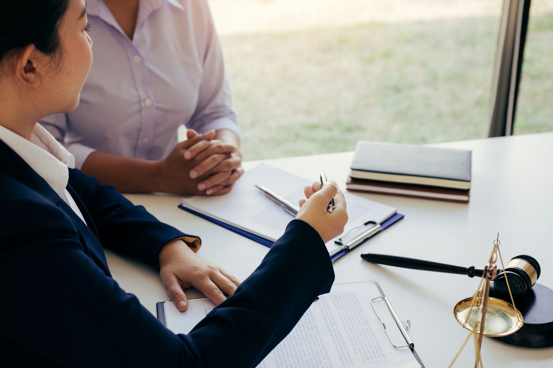 A person in a business suit gestures while discussing documents with another individual at a table with a judge's gavel.