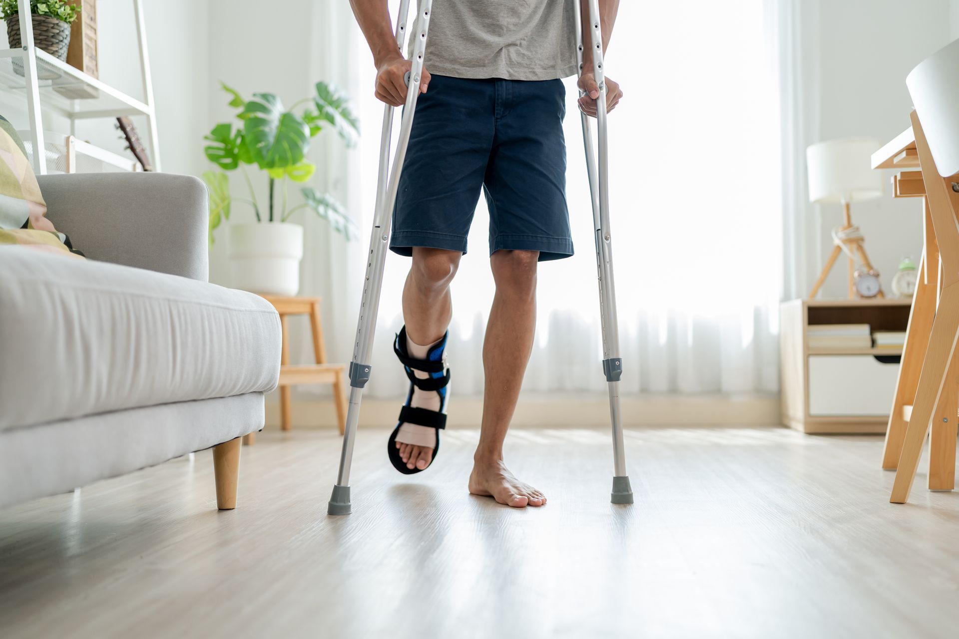 A person with a leg brace standing in a brightly lit room using crutches for support.