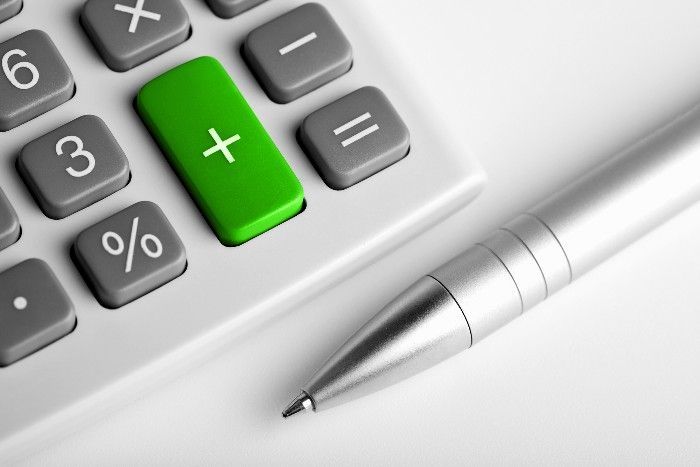 Calculator with a green plus button, silver pen lying next to it.