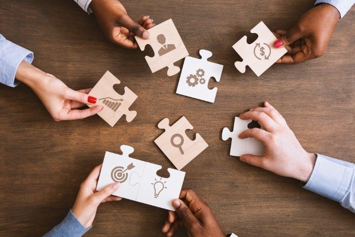 Hands holding puzzle pieces with icons, symbolizing teamwork and collaboration.