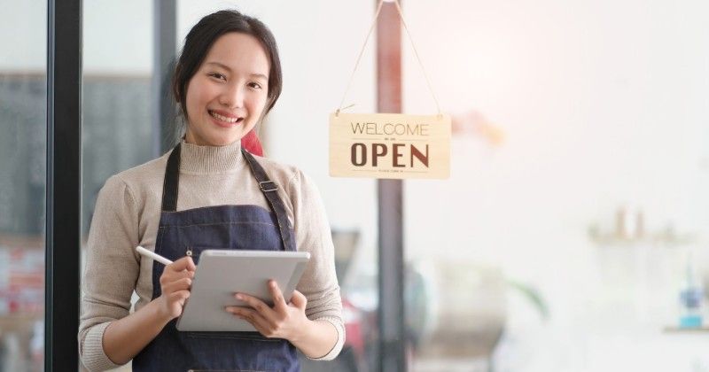 Woman in apron holding tablet, smiling in front of an