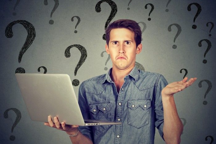 Man with laptop shrugs, confused. Question marks on background.
