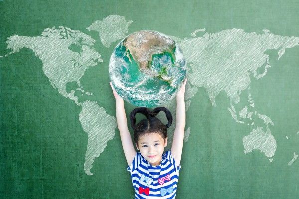 Girl holding a globe in front of a chalk world map, smiling, against green chalkboard.