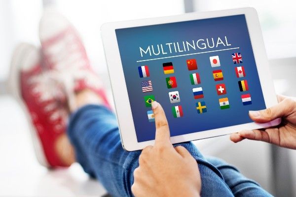 画面に「MULTILINGUAL」と表示され、その文字の下に多くの国の国旗が表示されているタブレットを使用している人。
