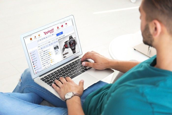 Man seated with laptop, shopping online at a website, wearing jeans and a watch.