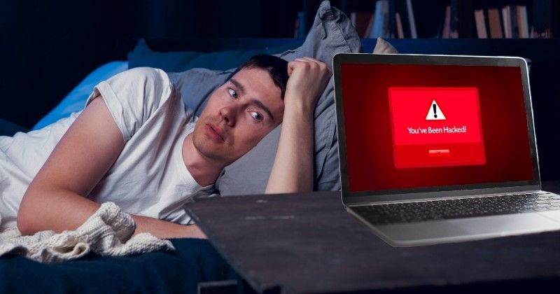 赤いエラー画面が表示されたノートパソコンを見つめる男性。夜、ベッドで枕に腕を乗せている。