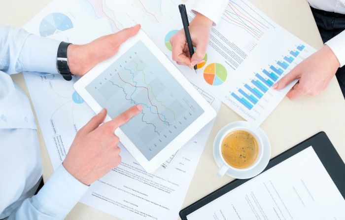 People reviewing financial data on a tablet and paper documents, with coffee.
