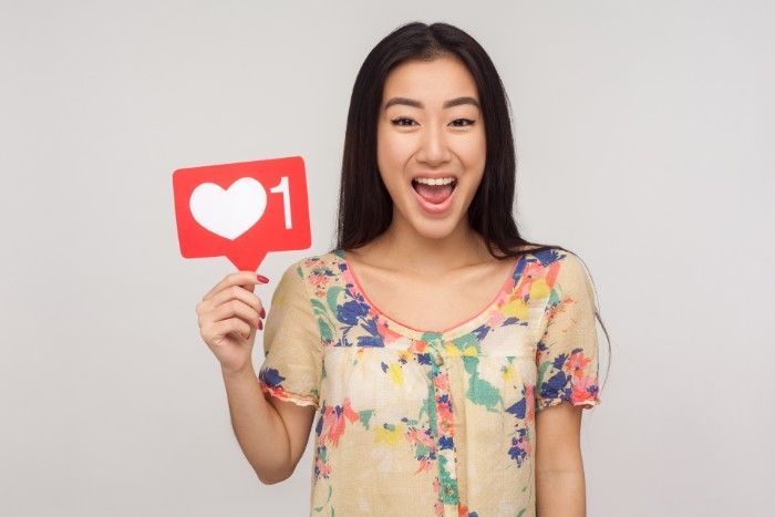 Woman with long black hair, smiling widely, holding a red social media 