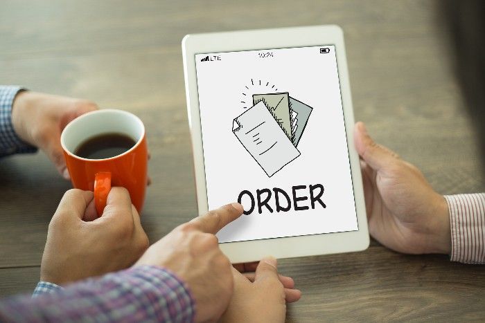 Two people looking at a tablet displaying an order icon and the word