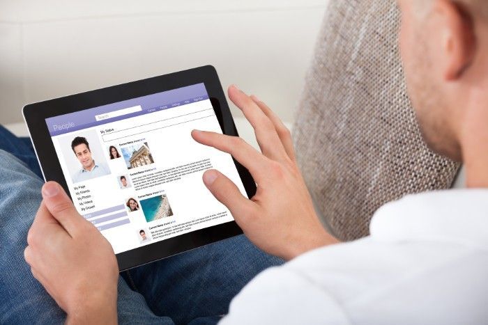 Person using a tablet, scrolling through a social media page; interior setting, daytime.