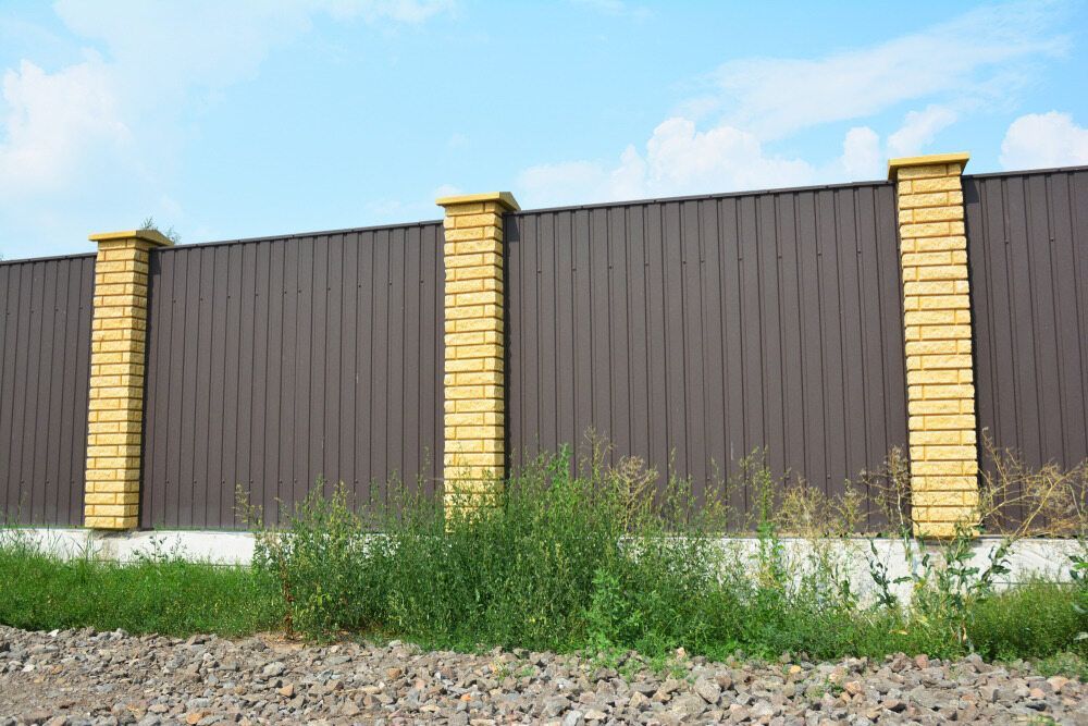 A Brown Fence With Yellow Pillars is Surrounded by Grass and Gravel — Lakecrest Projects in Lake Macquarie, NSW