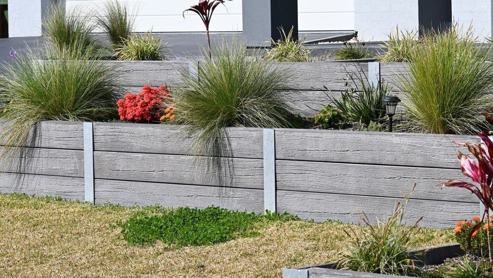 A Wooden Retaining Wall With Plants and Flowers in Front of a House — Lakecrest Projects in Belmont North, NSW