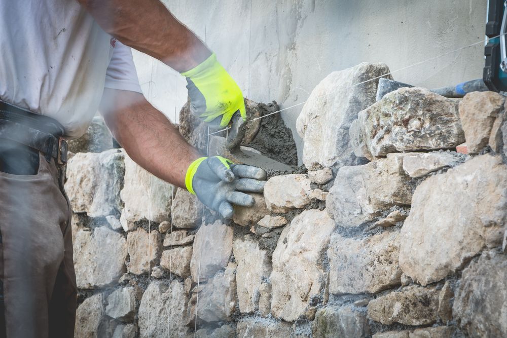 A Man is Building a Stone Wall With a Trowel — Lakecrest Projects in Belmont North, NSW
