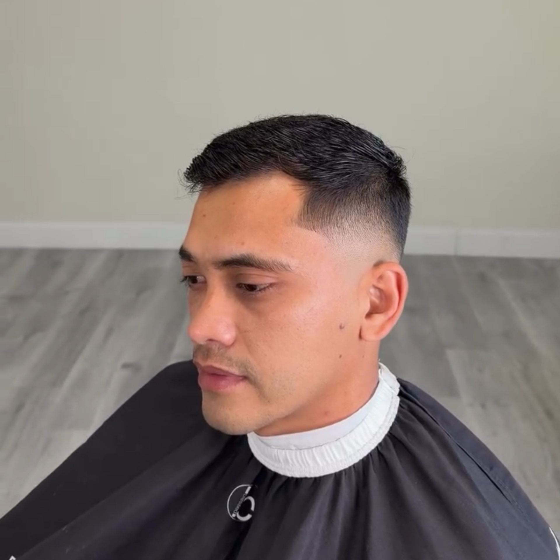 A close-up shot of a person with a short, professional faded haircut, wearing a barber’s cape in a salon setting.