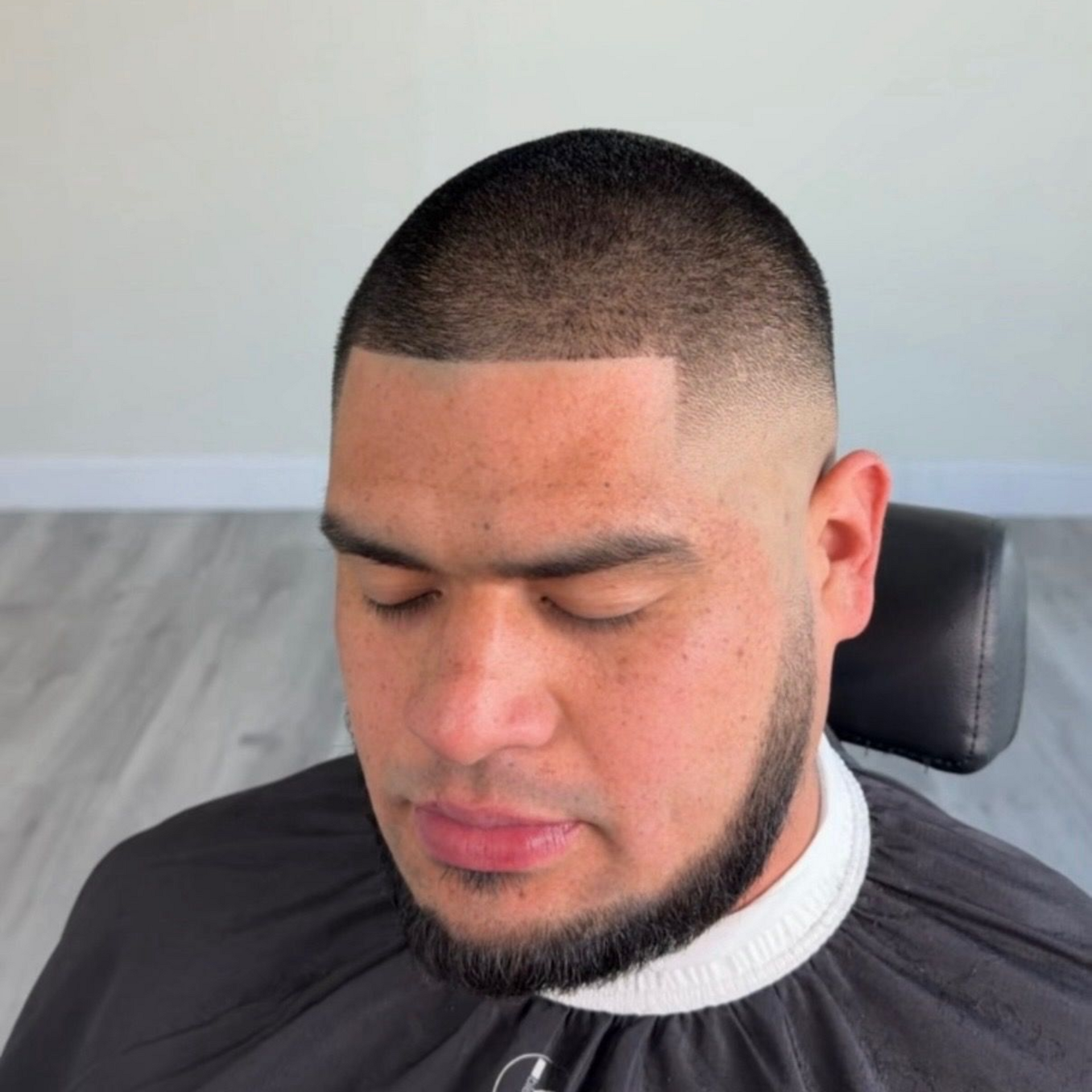 A man with a close-cropped haircut featuring a sharp, clean fade and lined forehead, wearing a black barber cape.