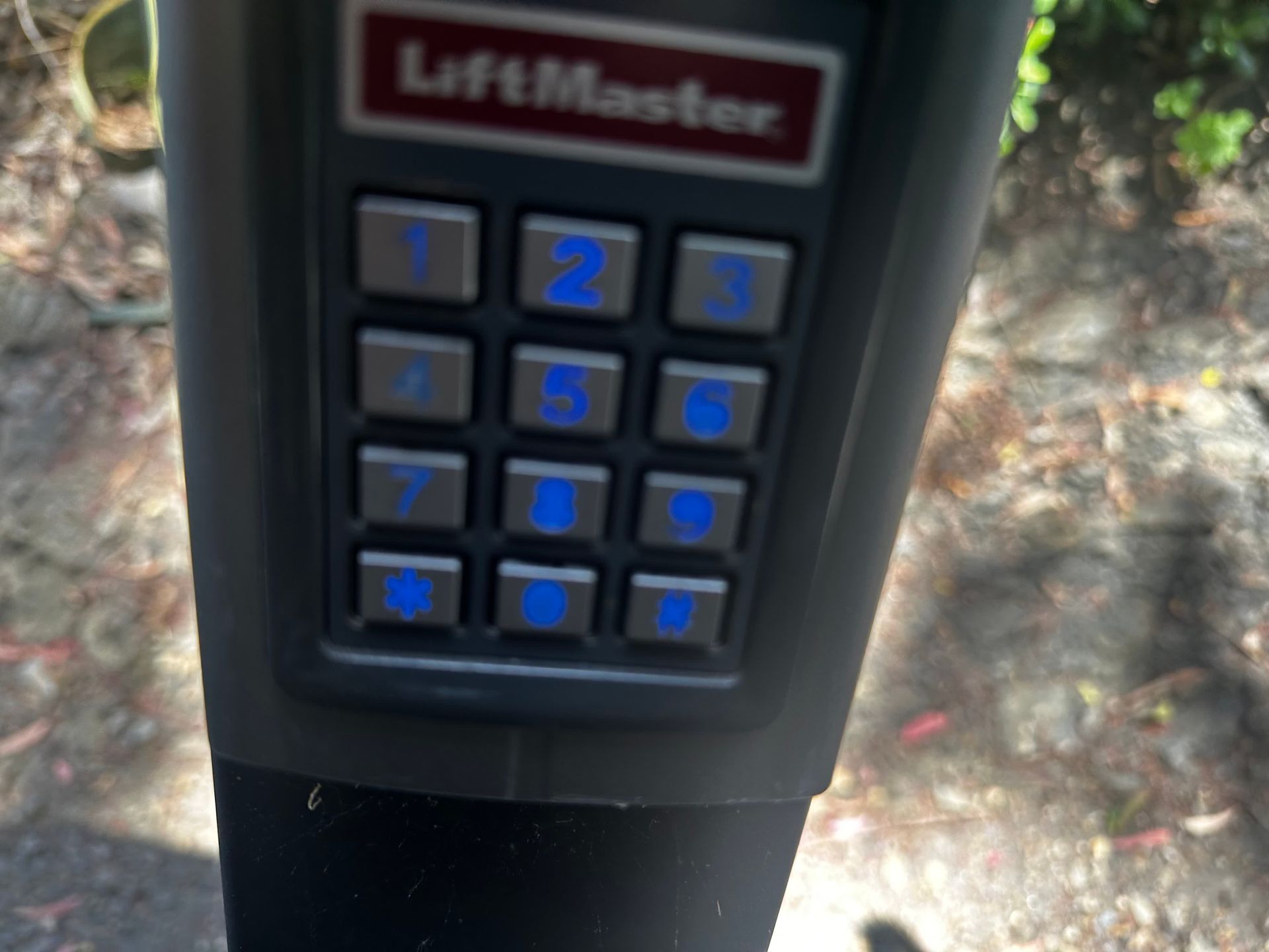 A LiftMaster keypad with illuminated blue numbers.
