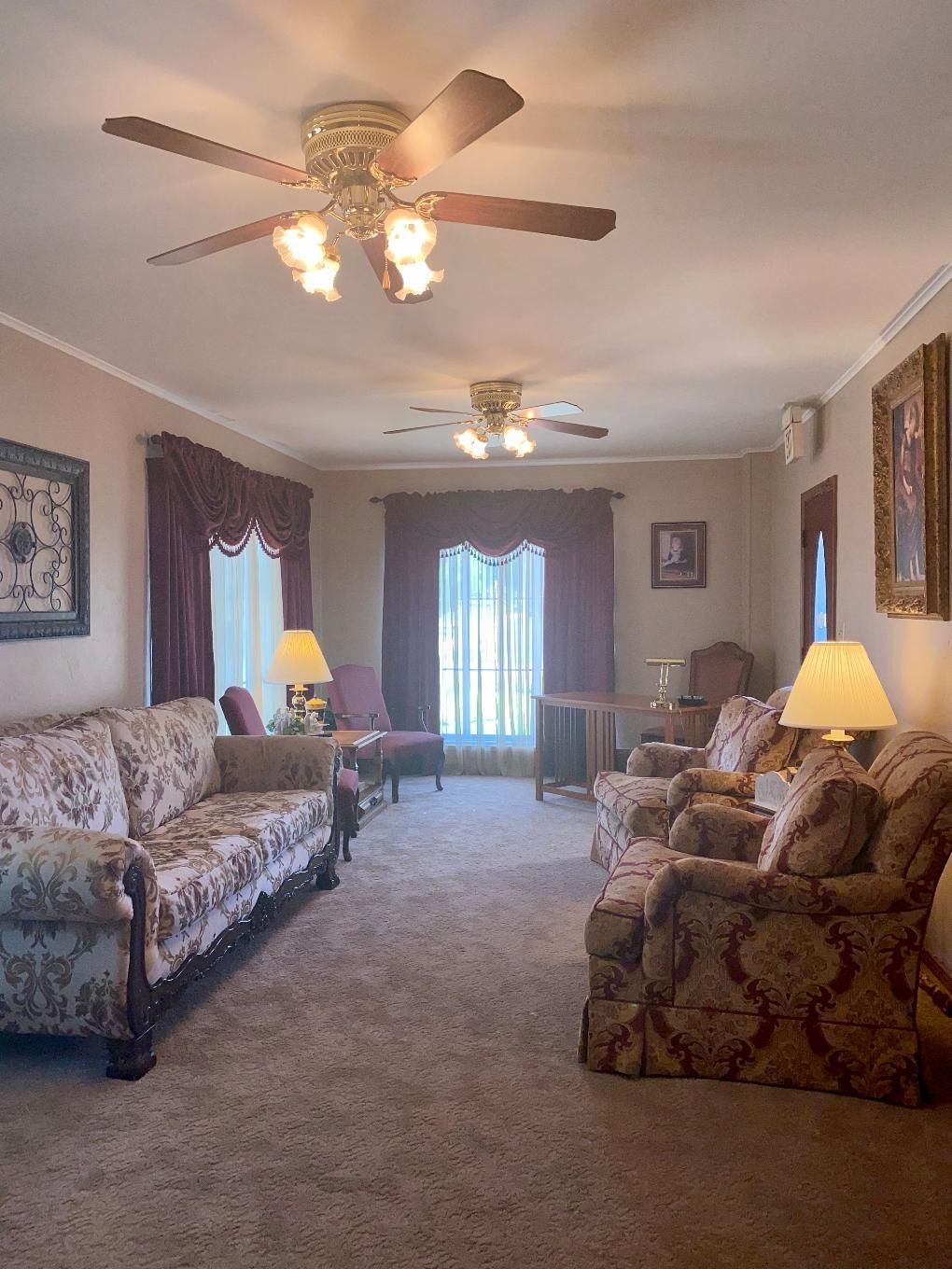 Cozy room with maroon curtains, chandelier, wooden doors, armchair, and side table with lamp.