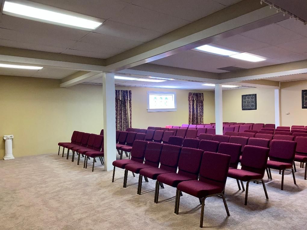 Empty auditorium with rows of burgundy chairs, beige walls, and a light beige carpet.