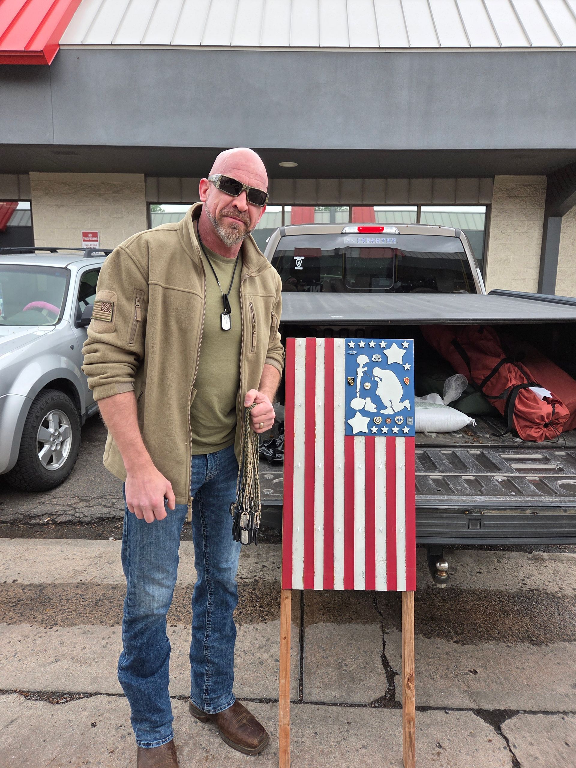 A man is standing in front of a truck holding an american flag.