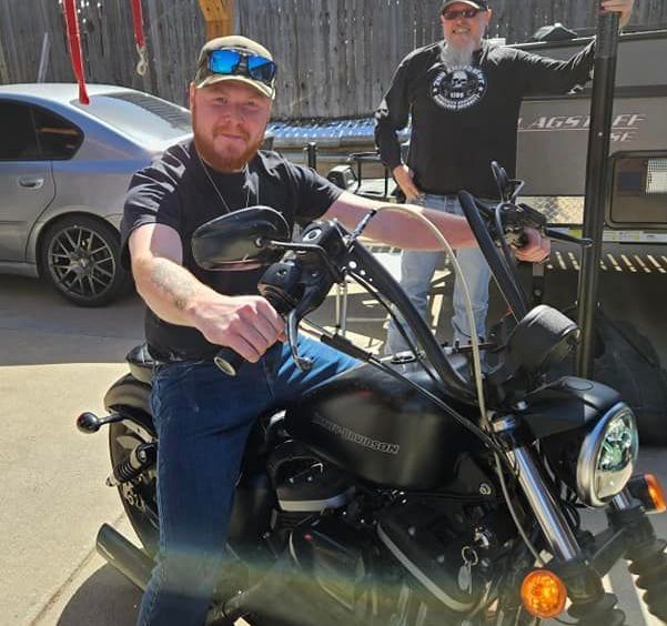 Two men are standing next to a black harley davidson motorcycle