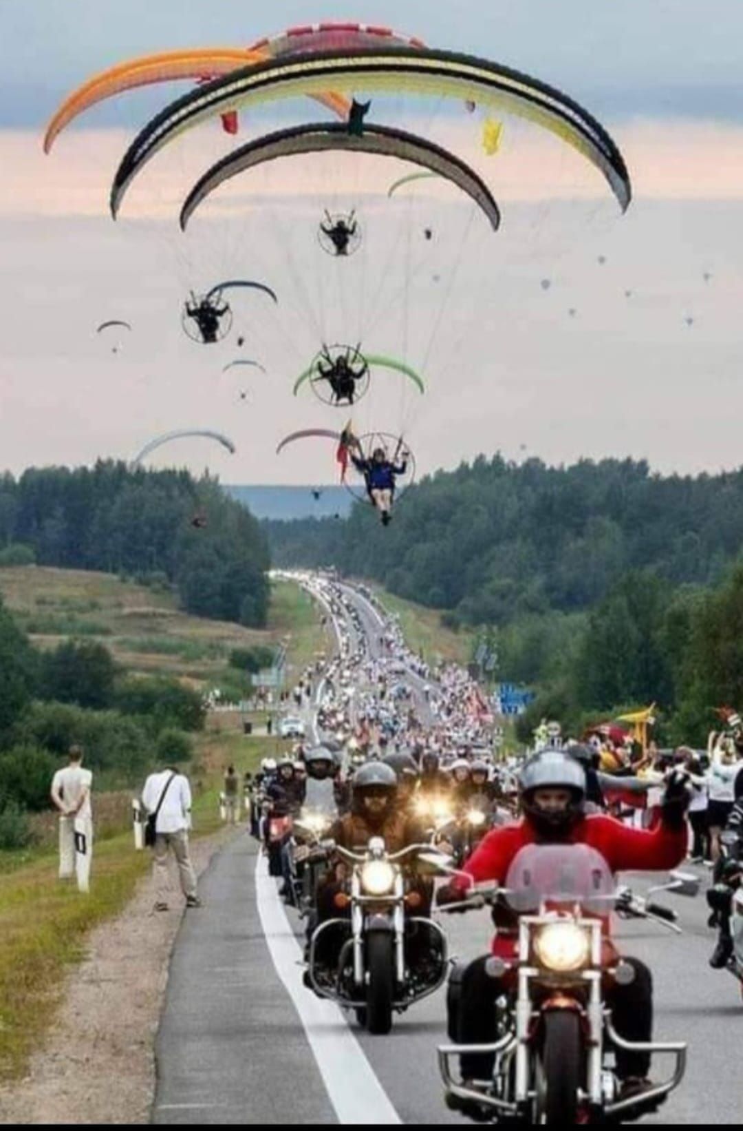 A group of people riding motorcycles down a road with parachutes in the background