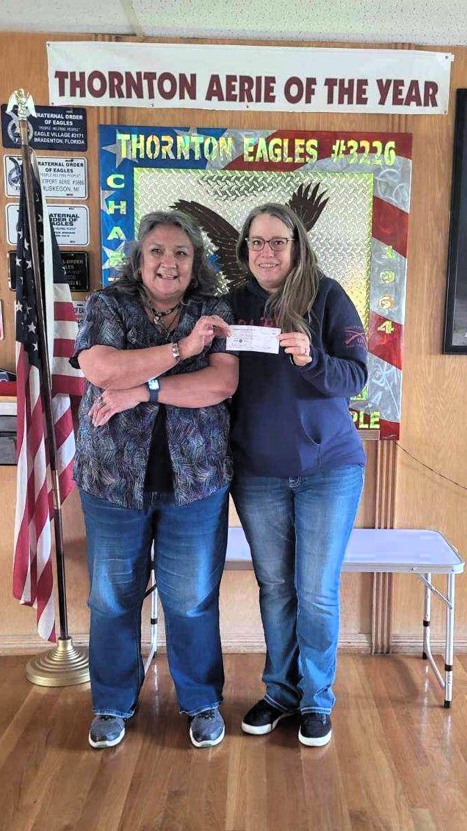 Two women are standing next to each other in front of a sign that says thornton aerie of the year.