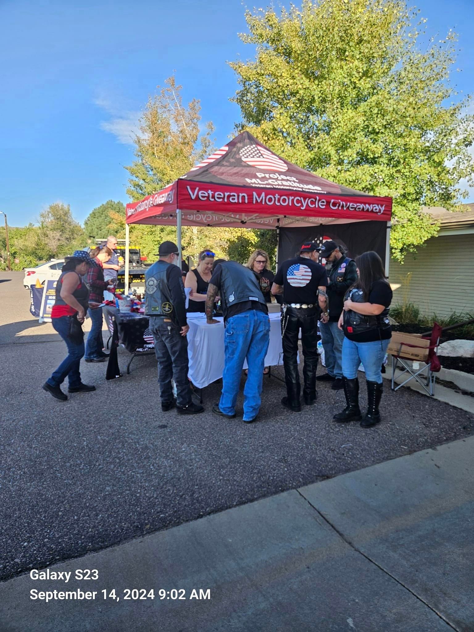 A group of people are standing under a tent in a parking lot.